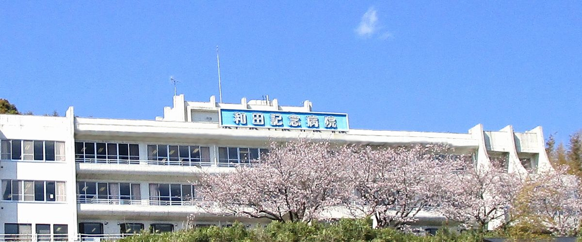 白い建物と桜の木が映る介護施設の外観。施設名の看板が見える。